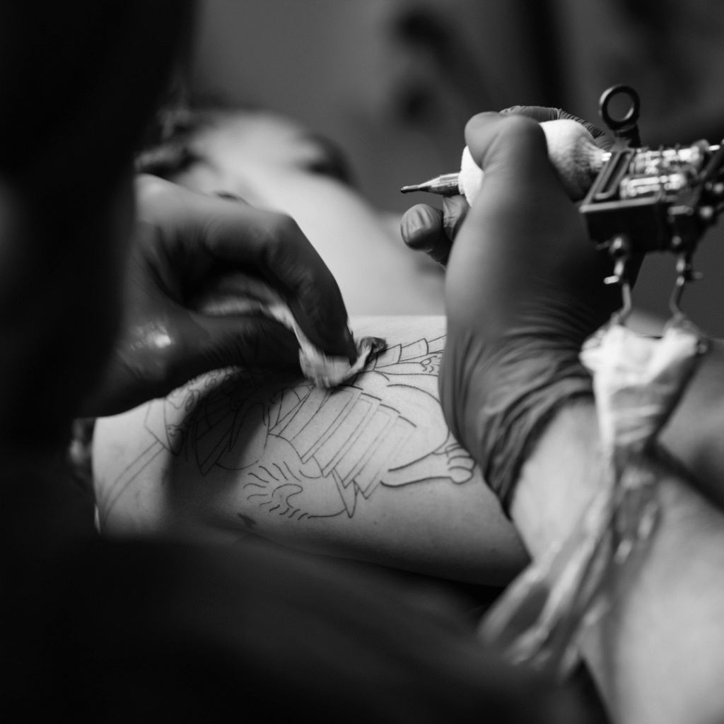 Close-up of a tattoo artist’s gloved hands outlining a design, wrist angled for steady control.
