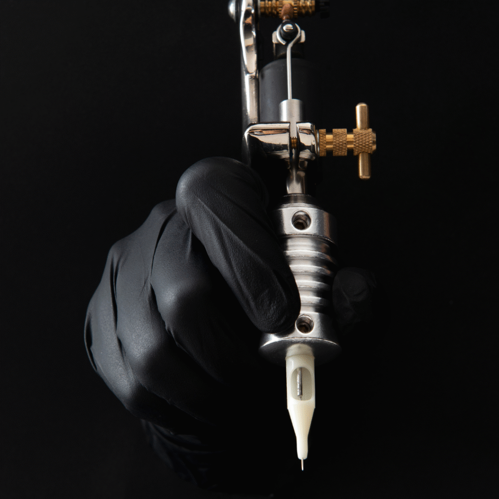 Gloved hand gripping a fine line tattoo pen with a slender needle tip against a black background.