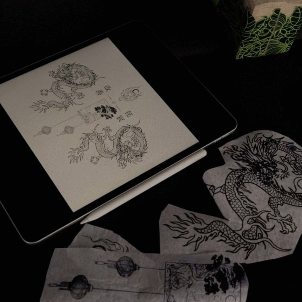 Digital tablet showing detailed dragon tattoo designs alongside printed stencils on a dark workstation.