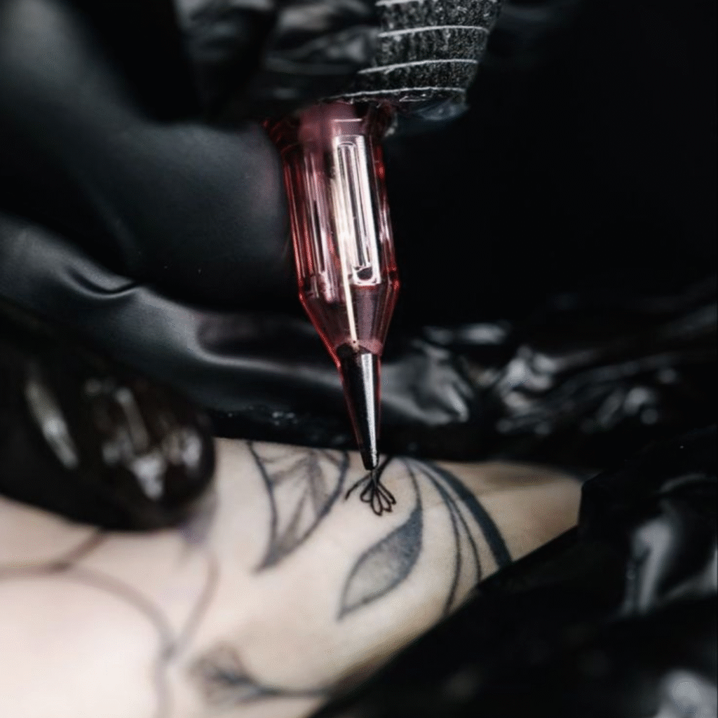 Close-up of a red cartridge tattoo machine in black-gloved hands outlining a floral design on skin.