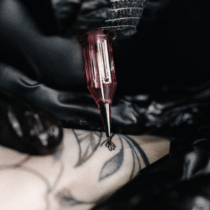 Close-up of a red cartridge tattoo machine in black-gloved hands outlining a floral design on skin.