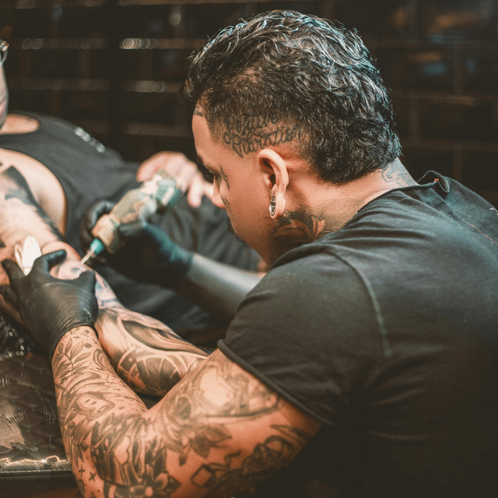 Tattoo artist with full arm tattoos working on a client’s arm inside a modern studio.