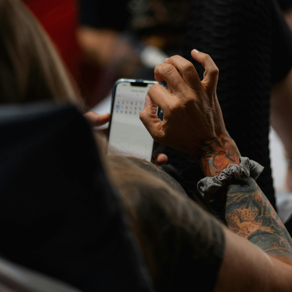 Tattooed artist using a phone calendar to book a session, representing the use of a tattoo appointment scheduler.
