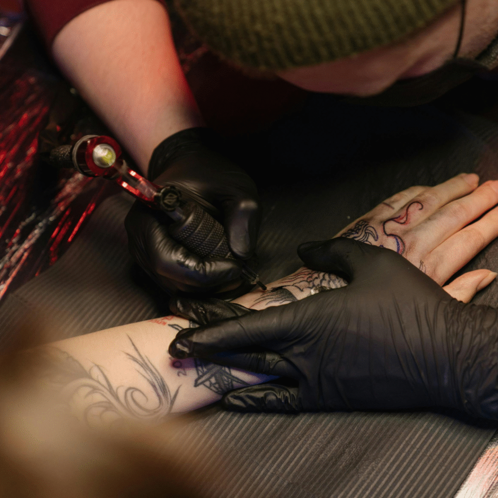Tattoo artist using a rotary machine to ink a client’s forearm, illustrating tattoo business growth through consistent bookings.