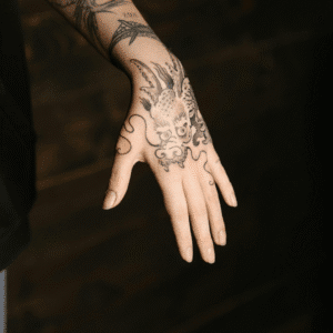 Close-up of a tattooed hand featuring a detailed dragon design, illustrating the need for effective tattoo artist booking tools to manage high-value clients.