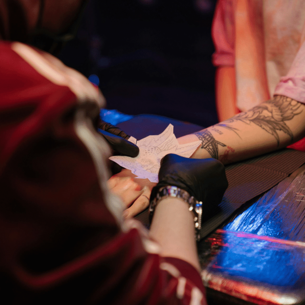 Tattoo artist in black gloves carefully presses a floral stencil onto a client’s forearm, preparing for precise needle work.