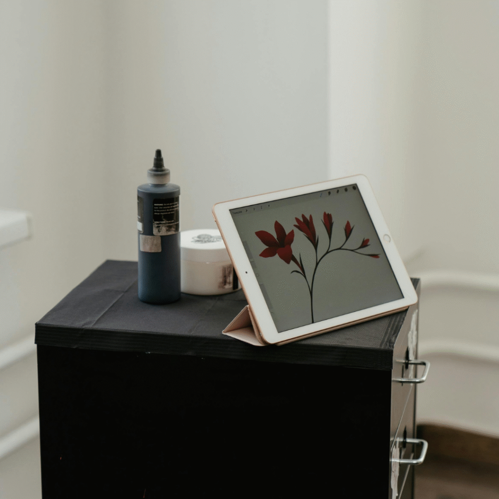 Tablet displaying a red floral tattoo design resting on a black equipment case, beside a bottle of tattoo ink in a bright studio.