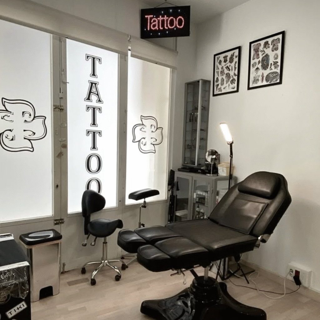 Empty tattoo studio setup featuring a black adjustable tattoo chair, artist stool, ink cabinet, and wall-mounted flash art in a clean, light-filled room.