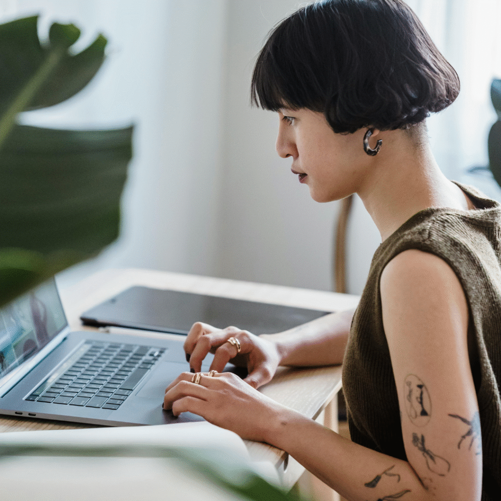 Tattooed artist working on a laptop, creating client referral ideas for their tattoo studio.