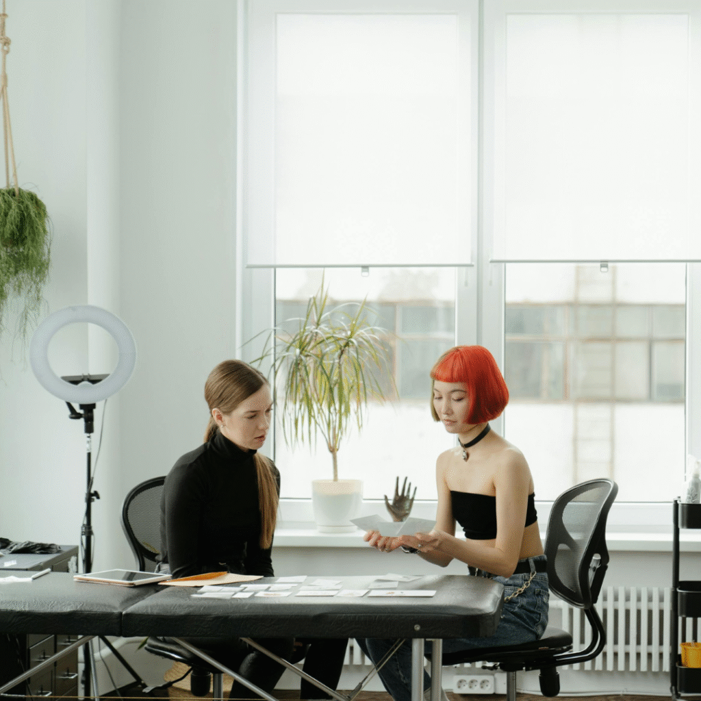 Tattoo artist consulting with a client at a studio table, discussing design ideas and booking details.