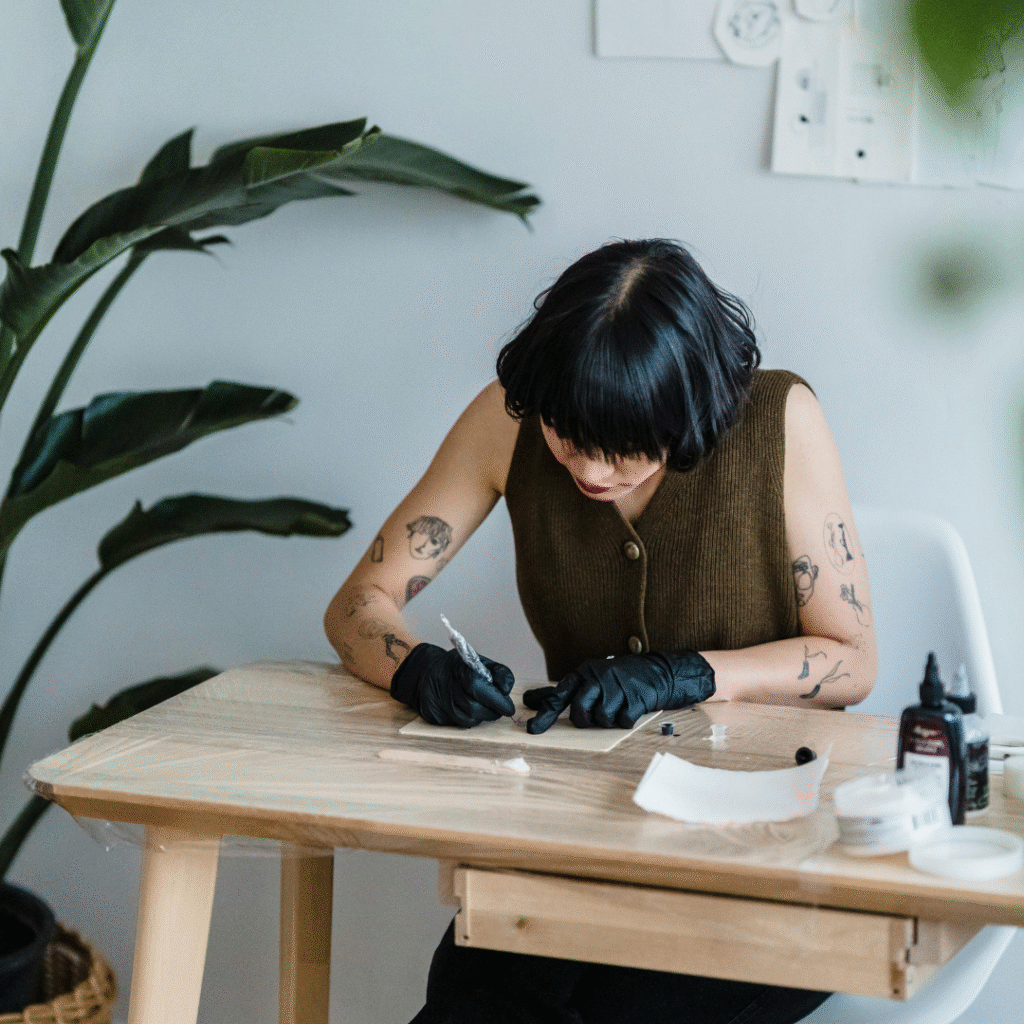 Tattoo artist wearing gloves, preparing tools and sketching designs at a studio desk.