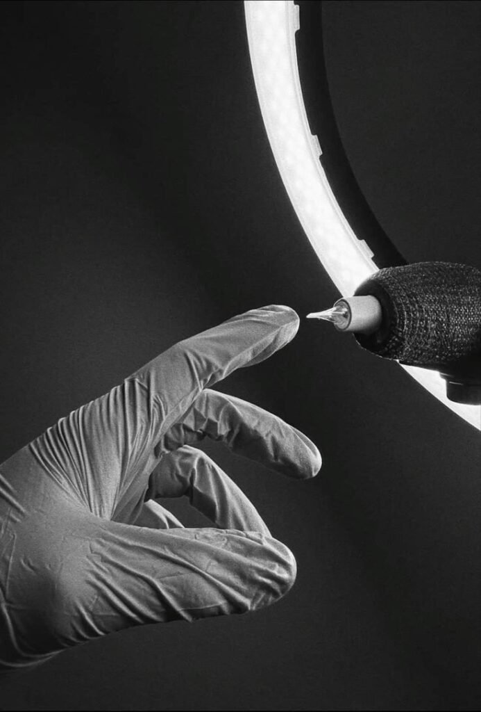 Tattoo machine needle with gloved artist hand under ring light