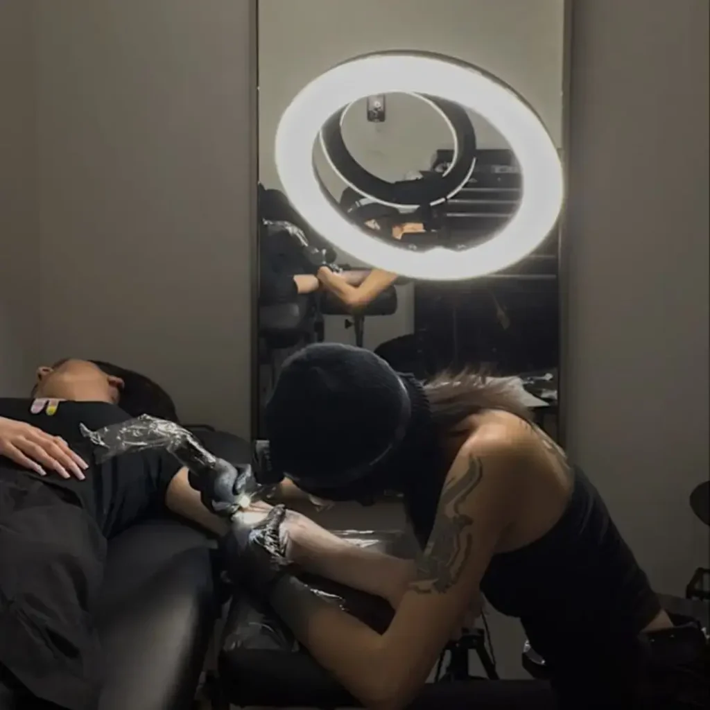 Tattoo artist creating arm tattoo under ring light during late-night studio session