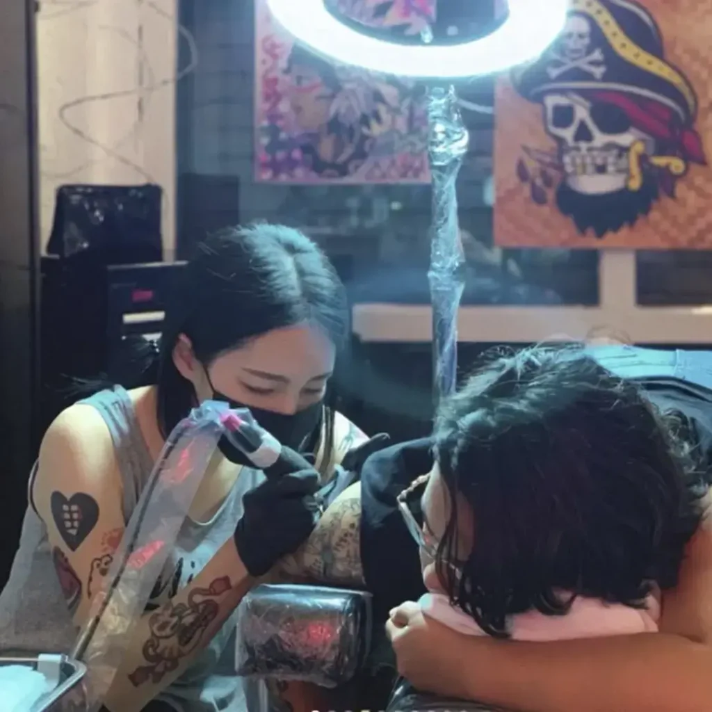 Tattoo artist focused on leg tattoo design under bright ring light reflection