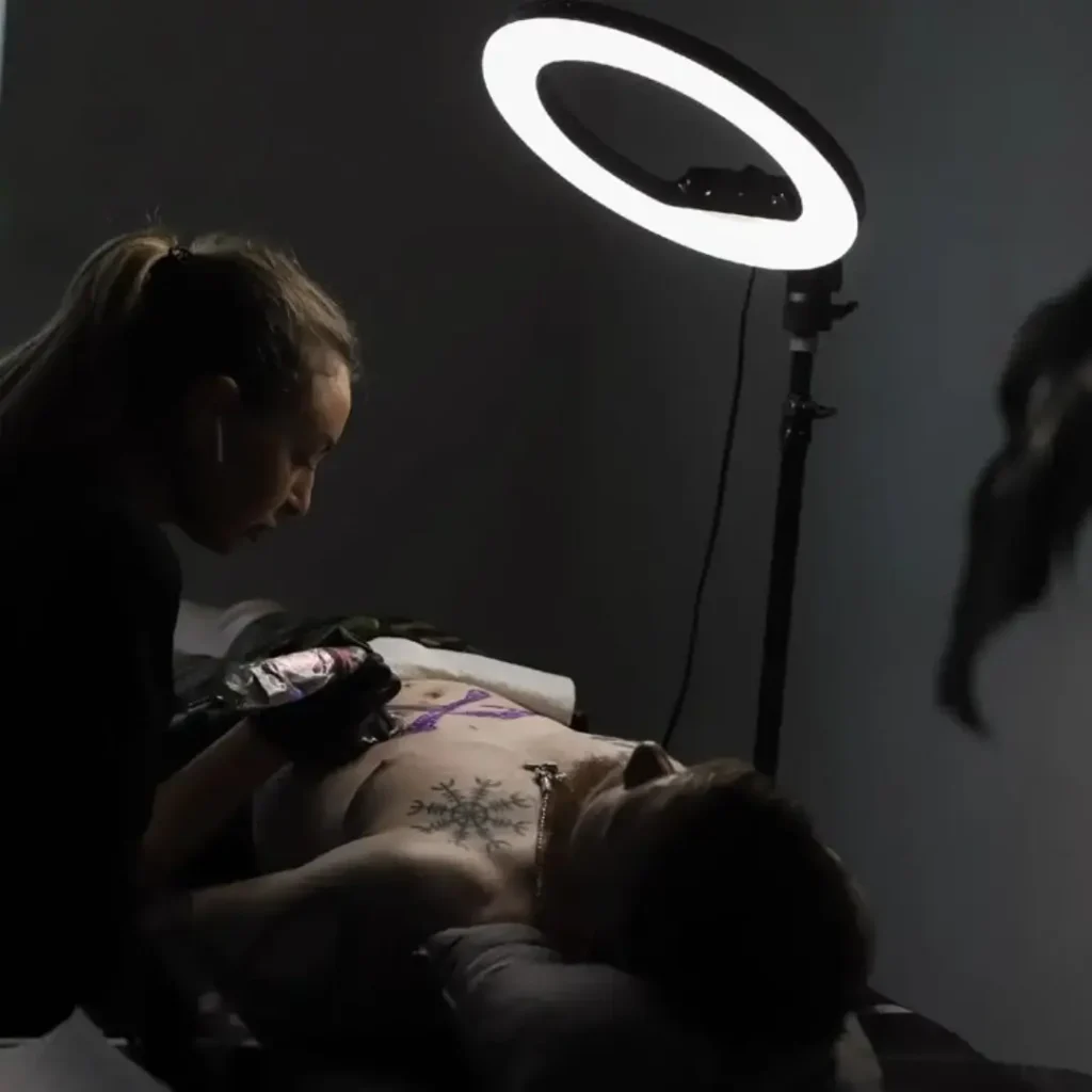 Tattoo artist working under ring light on client’s chest in a modern tattoo studio