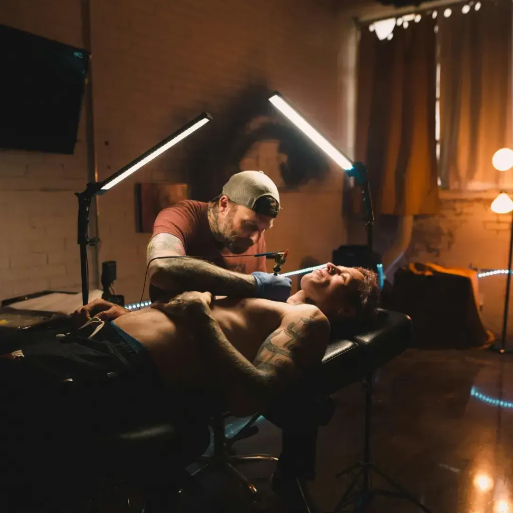 Tattoo artist working on client’s chest tattoo under professional lighting setup