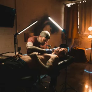 Tattoo artist working on client’s chest tattoo under professional lighting setup