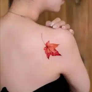 Realistic maple leaf tattoo on shoulder in warm tones – fall tattoo trends 2025