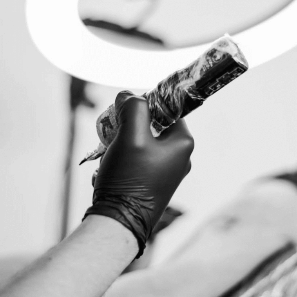 Tattoo artist holding tattoo machine wrapped in plastic under bright ring light