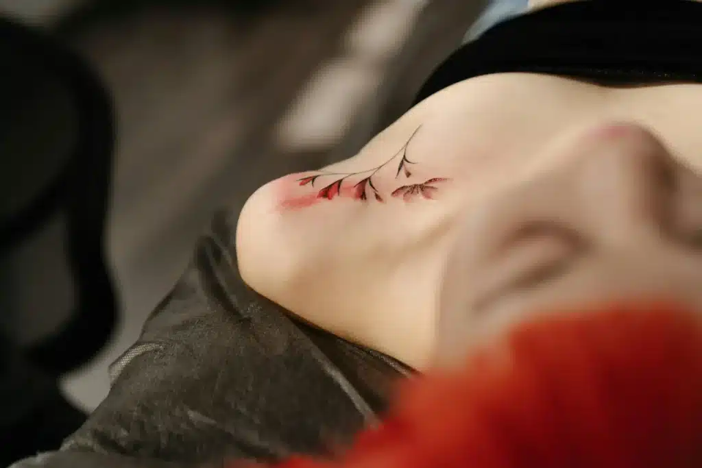 Fine-line floral tattoo with red shading freshly done on client’s shoulder