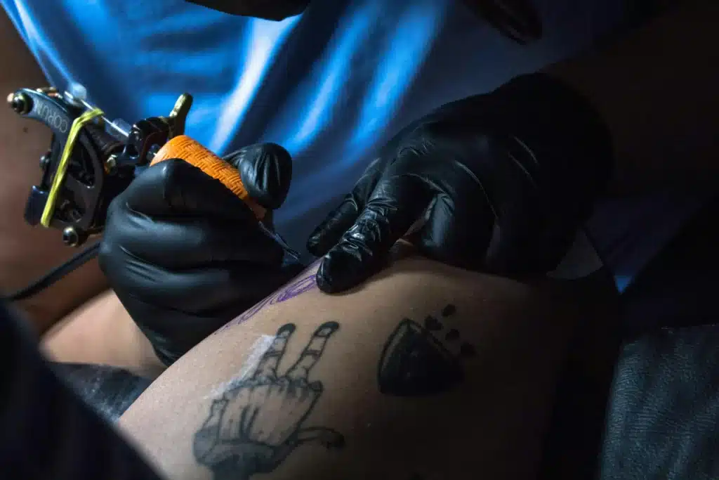 Tattoo artist using tattoo machine with black gloves during detailed linework session