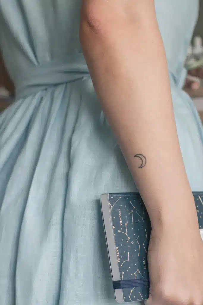 Minimal crescent moon tattoo on arm symbolizing calm and reflection – fall tattoo trends 2025