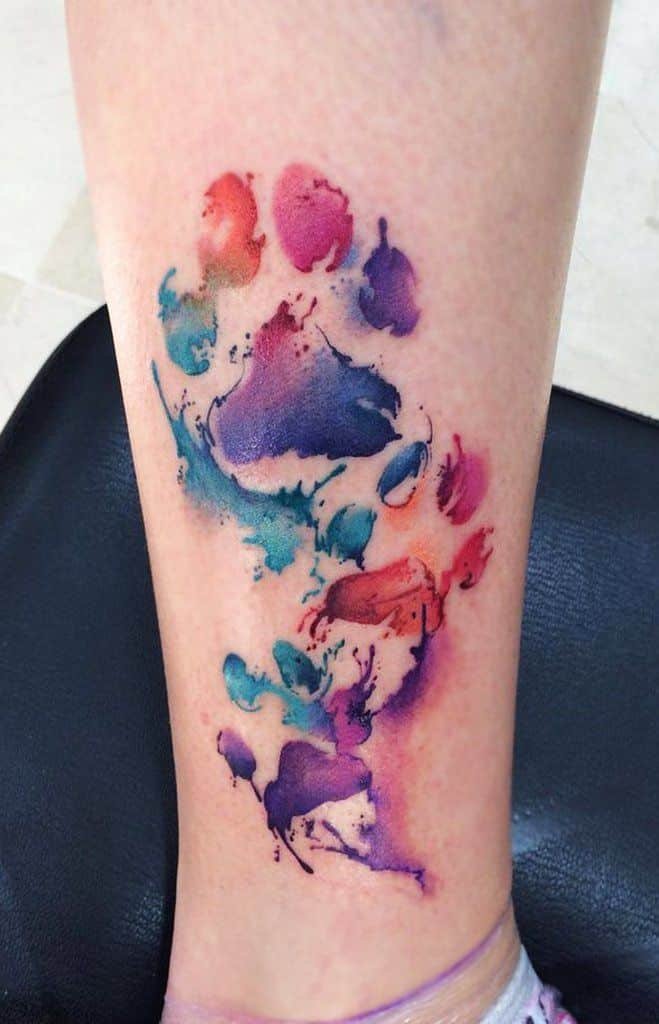 vibrant watercolor paw print tattoo with multicolor splashes on leg