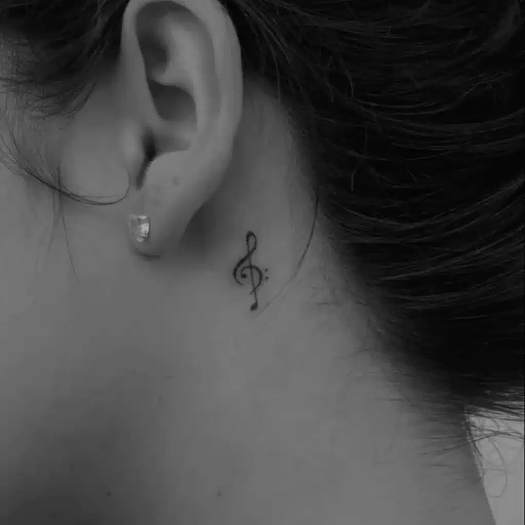 tiny treble clef music-inspired tattoo behind ear