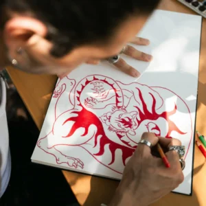 tattoo artist sketching japanese mythology-inspired tiger design on paper