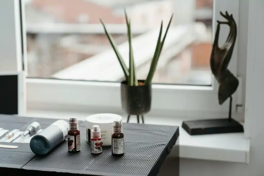 Tattoo ink bottles and tools arranged neatly on a studio table with a window in the background, showing a quiet workspace during the holiday rush.