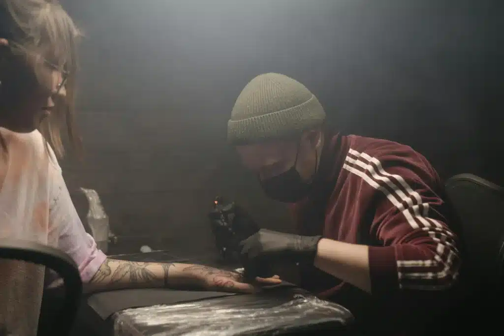 Tattoo artist focused on tattooing a client’s arm inside a dimly lit studio, representing precision, focus, and creative dedication.