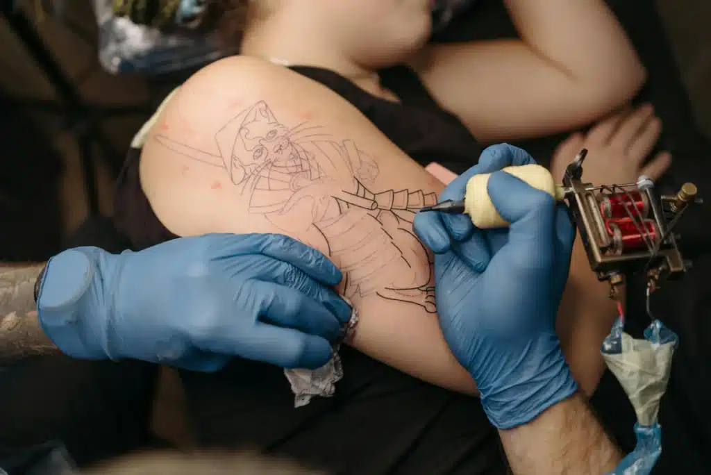 Tattoo artist outlining cat tattoo design while managing appointments through tattoo booking by text