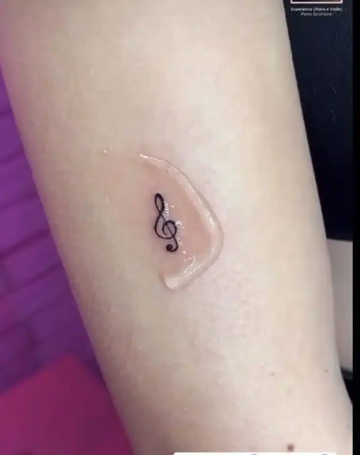 small treble clef tattoo on arm for minimalist music-inspired tattoo idea