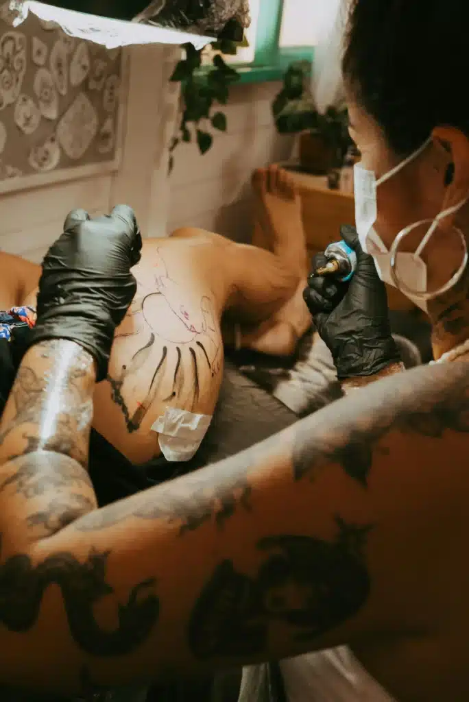 Tattoo artist in gloves adding color to a detailed leg tattoo during a session.